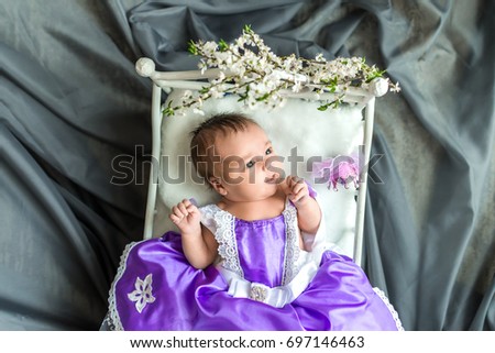 Newborn baby girl princess in purple dress with crown lying on soft white little bed