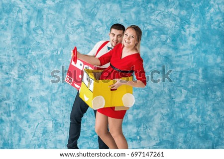 Side view shoot of a young couple moving in a toy paper cars. Studio photo
