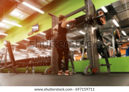 Gym background. Blurred picture of female exercising with barbell in modern fitness center.