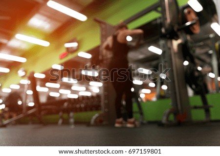 Gym background. Blurred picture of female exercising with barbell in modern fitness center.