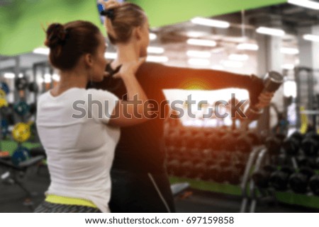 Gym background. Blurred picture of female exercising with weights with assistance of personal coach in modern fitness center.