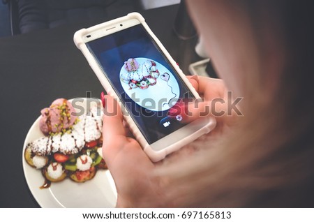 The girl takes pictures of dessert from wafers, ice cream and fruit
