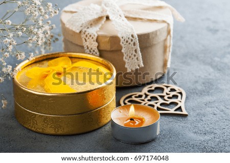Hand crafted golden gift with bow, lit candle on concrete background