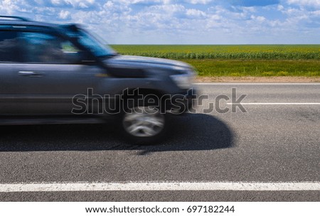 Photo of summer road. On the road are one blurry car, the weather is cloudy