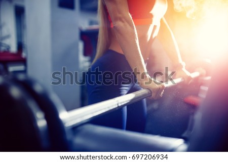 Close-up of a girl holding her hands with a barbell for pulling, squatting, fitness in the gym. Concept sports, toned picture, copyspace for text. Glare of sun and light.
