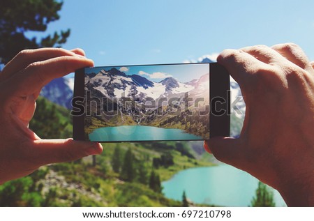 smartphone in hand photographing a mountain lake in the dolomites