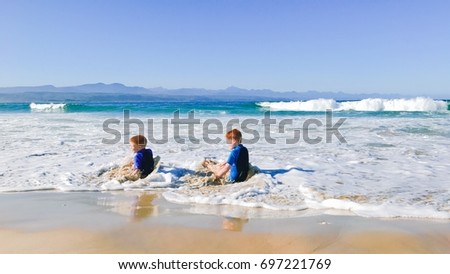 Two young boys playing in the surf of beautiful ocean with mountains in background