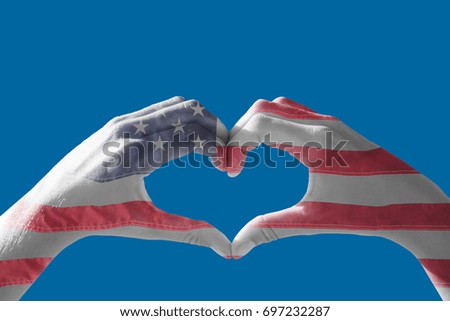 Hands making heart shape on the beach against american national flag with stars and stripes