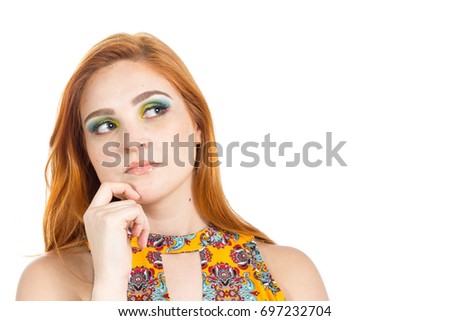 Green-eyed girl has a doubt, she looks to the side and evaluates. Fashion and colorful makeup. Redhead teenager wears vibrant yellow dress and floral patterns. Summer and tropical. White background.