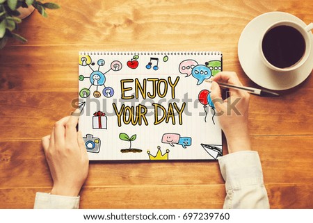Enjoy Your Day text with a person holding a pen on a wooden desk