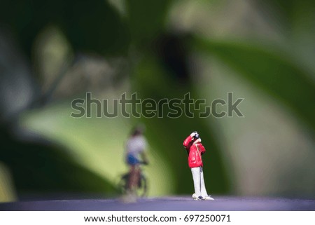 Closeup image of small photographer and bicycle rider model figures on wooden floor with blur green nature background