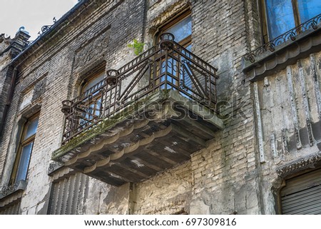 Ruined facade of the old building, with windows and balcony with metal fence