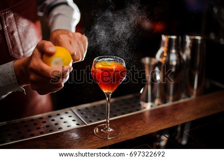 Bartender is adding lemon zest to the red cocktail at bar counter. Selective focus Royalty-Free Stock Photo #697322692