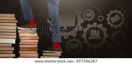 Low section of boy climbing stack of books against blackboard