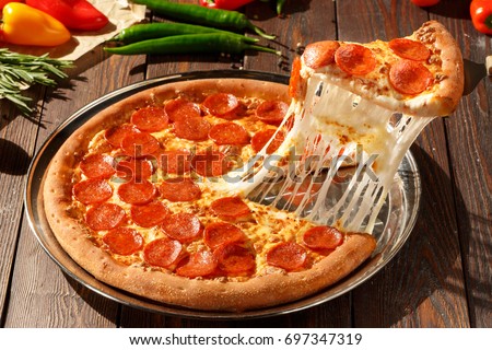 American pizza with pepperoni, mozzarella and tomato sauce. Pizza on a wooden table, morning, dawn.