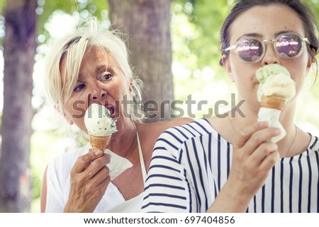 Modern mom and young daughter eating ice cream sitting on a deckchair in a water park on summertime. Concept of beautiful people having fun in summertime