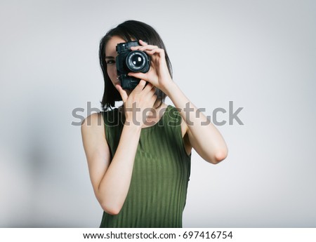 Beautiful young woman photographing on retro camera isolated on gray background