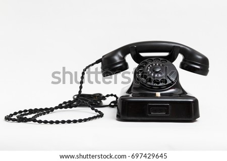 Old vintage stationary shiny black plastic telephone with round dial and a tube on the wire with a long cord on white background