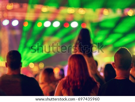 Blurred Youth Music Festival of pop music. Laser show on the stage. The crowd of fans. Silhouette of a little girl sitting on dad's shoulders. Blurred bokeh basic background for design