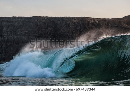 A green wave breaks in front of a cliff.