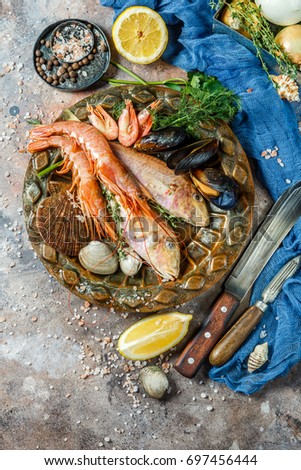 Photo of fish, shrimp, shellfish on ceramic plate at table with lemon, knives, shells