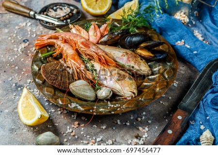Fresh sea fish, shrimp, clams on plate at stone table with knives, lemon