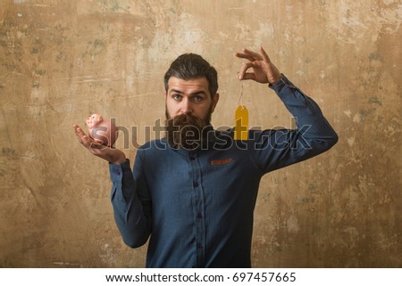 Man with beard on sad face. Guy hold shopping tag and moneybox. Loan and bankruptcy. Money and success. Businessman take bank credit.