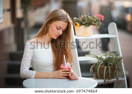 Close up portrait of a beautiful blonde girl sitting outdoor in cozy cafe in town. Pretty young model  looking down on a drink. Glowing light