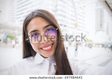 Pretty business woman take a self portrait with her smart phone outdoor, Asian nerdy glasses girl selfie with building background