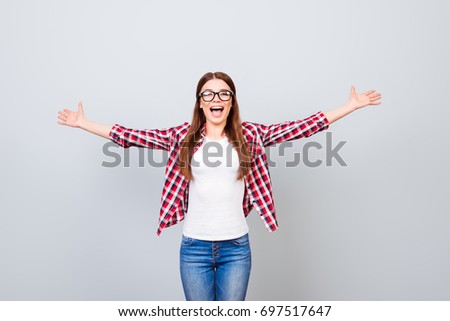 Cheerful young nerdy girl student is welcoming in university on pure background in glasses and casual outfit. She is gesturing victory, she passed exams