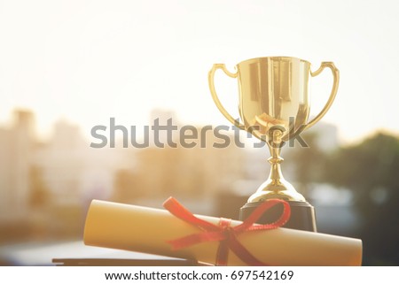 Champion golden trophy with Graduation certificate on city sunset time with copy space. Success and Education concept. Royalty-Free Stock Photo #697542169