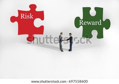 This photo is a financial concept for investing in the stock market, real estate, gold or commodities.  Two businessmen shake hands on a white background with risk, reward puzzle pieces behind them.