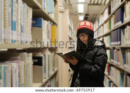 An Asian girl who is reading book in library, she is very concentrated.
