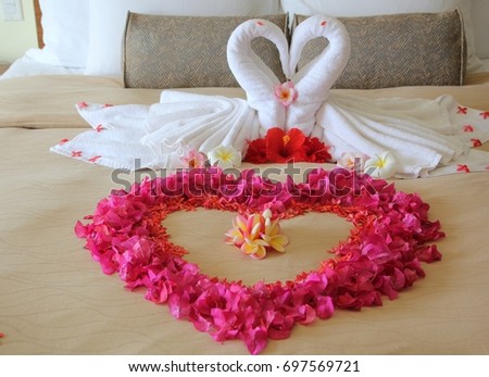 Close up of two white towel swans, with flowers shaped into a big heart on the bed of a honeymoon suite.