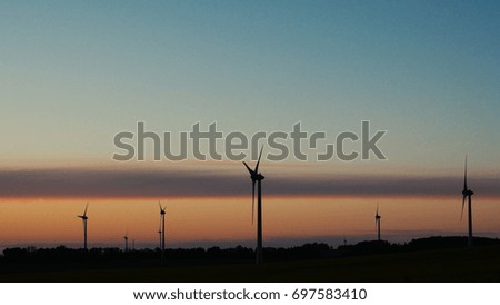 Wind turbines farms with rays of light at sunset in the background.
