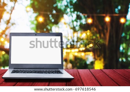 Laptop computer with white blank screen for presentation on wooden desk with abstract night light bokeh image at outdoor coffee shop at night, copy space, vintage tone, business technology concept