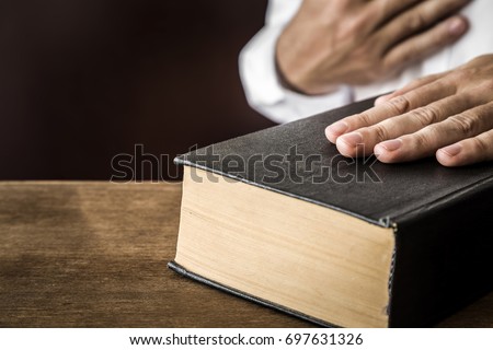 Man's hand swearing on the bible. Taking an oath.  Royalty-Free Stock Photo #697631326