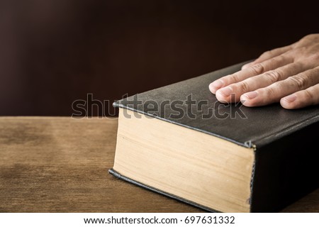 Man's hand swearing on the bible. Taking an oath.  Royalty-Free Stock Photo #697631332