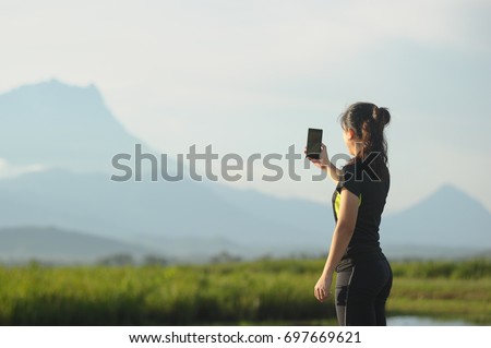 Sport young Asian woman runner taking picture using smartphone while doing running exercise at outdoor. Concept modern young active lifestyle.