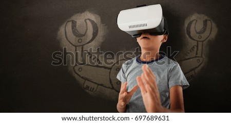 Boy gesturing while using virtual reality headset against blackboard