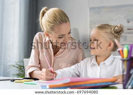 happy mother and daughter drawing together and smiling each other 