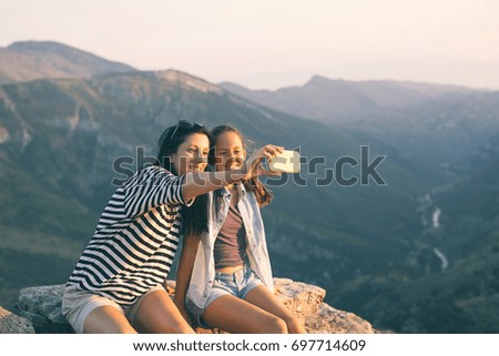 Mother and daughter photographing, taking a selfie on mountain peak, whilst resting