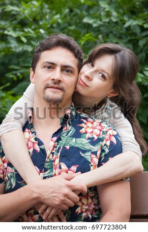 Charming couple of a man and woman sitting on the bench, woman embraces man