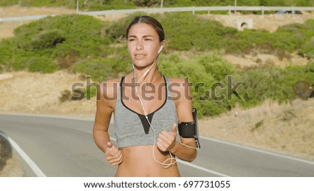 Portrait of a beautiful sportswoman running in the nature, smiling in sports clothes, listening to music on the phone, background of mountains. Concept: to love sports, run, burn calories, sporty body
