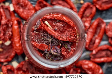 Jar with many dried red tomatoes and spices on a dark surface close up. Dried tomatoes texture blurred background. General top view