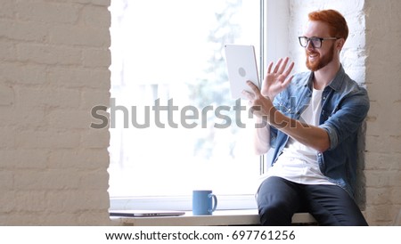 Man with Beard and Red Hairs Using Tablet for Video Chat, Skype, Face time Royalty-Free Stock Photo #697761256