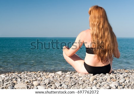 the girl sits on the seashore in the weakening pose in clear summer day