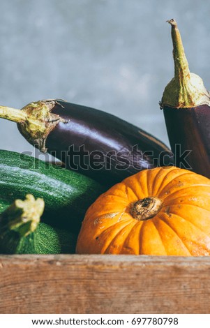 Autumn harvest in a wooden box, pumpkin, green zucchini and eggplant on a gray background