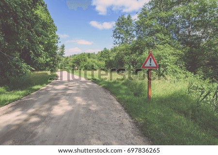 gravel road in sunny summer countryside with perspective and bright red attention sign - vintage film look