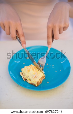Photo of cake on plate which woman cuts with help of fork and knife